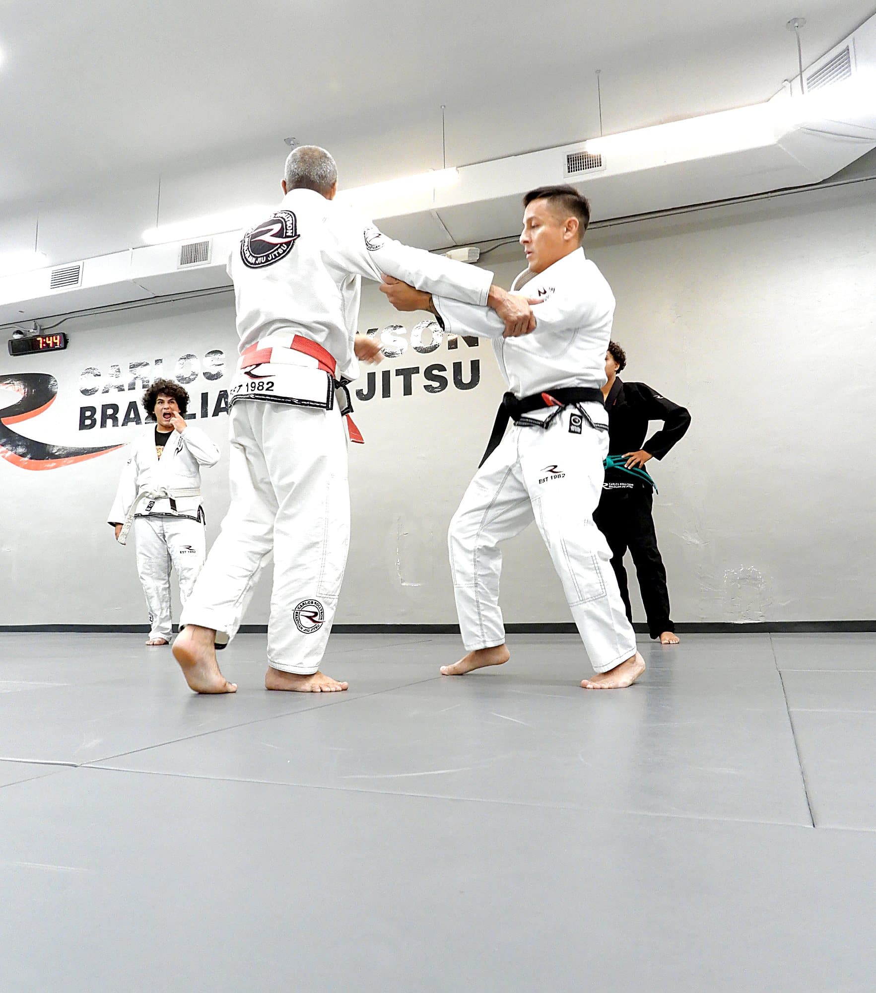 Master Carlos Rollyson demonstrating a throw on an adult student in front of the Rollyson logo wall