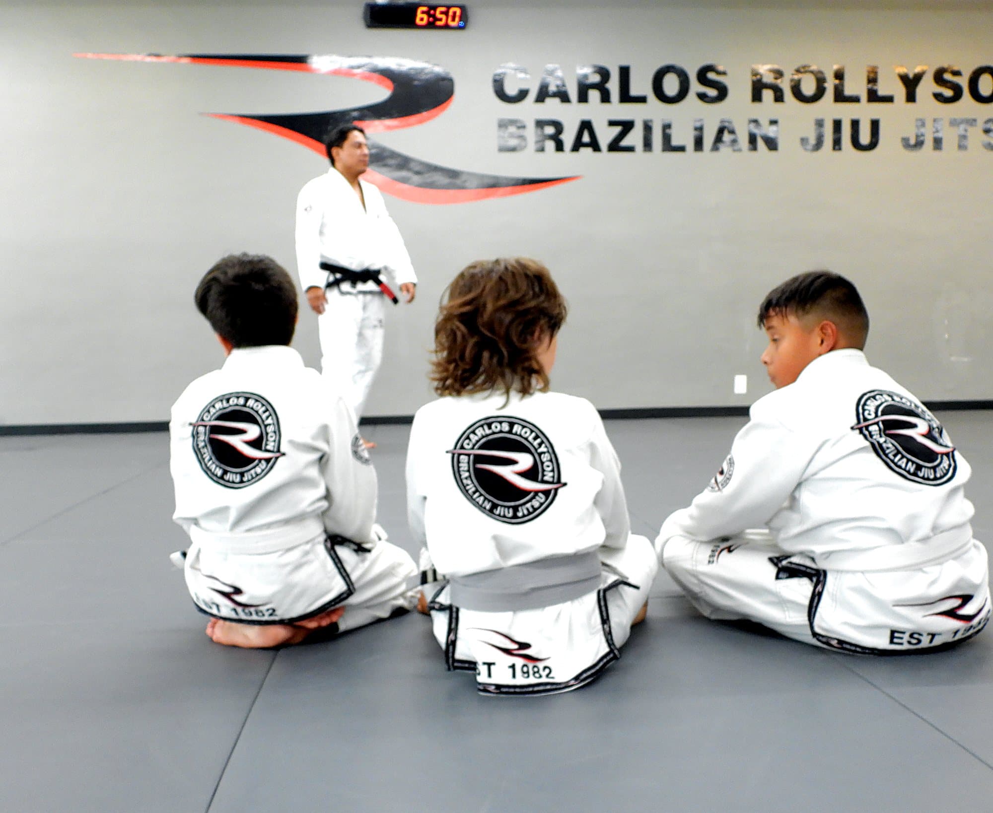 Kids Brazilian Jiu Jitsu class seated on the mat listening to their instructor